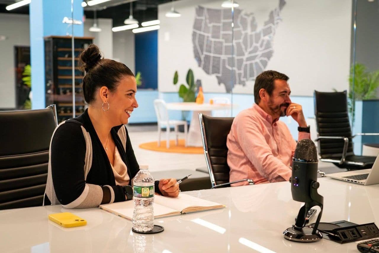 Ally and a colleague laughing during a partner call at the Conduit conference table, US map on the wall behind them