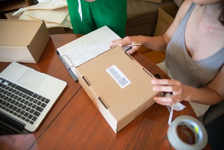 Two people packing online orders beside a laptop