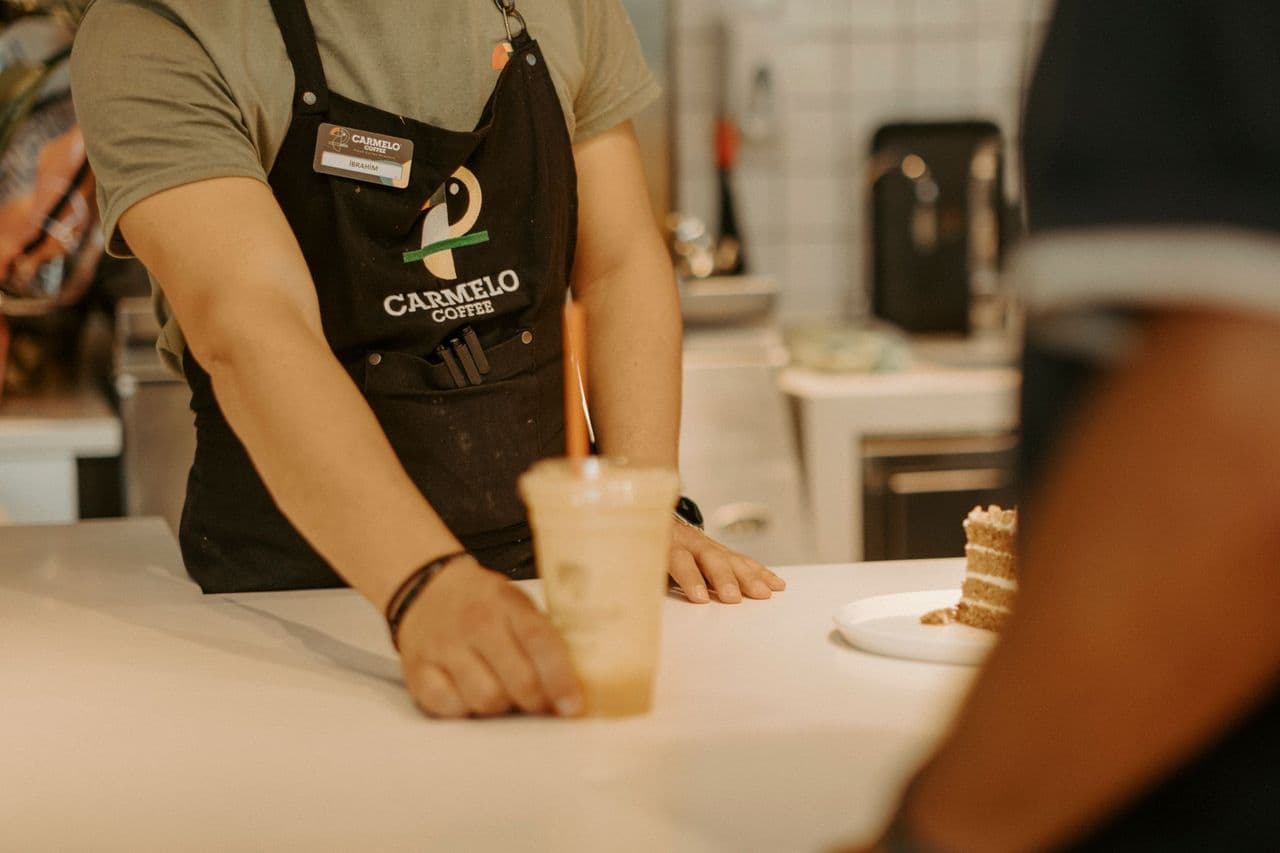 A barista handing an iced coffee across the counter