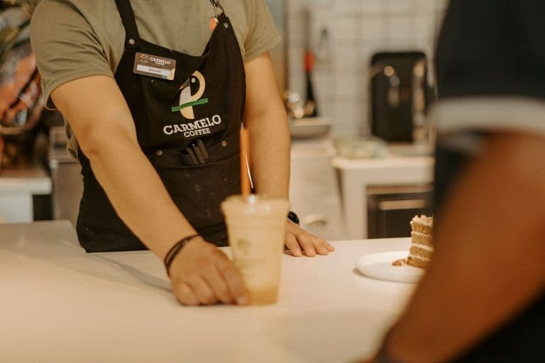 A barista handing an iced coffee across the counter