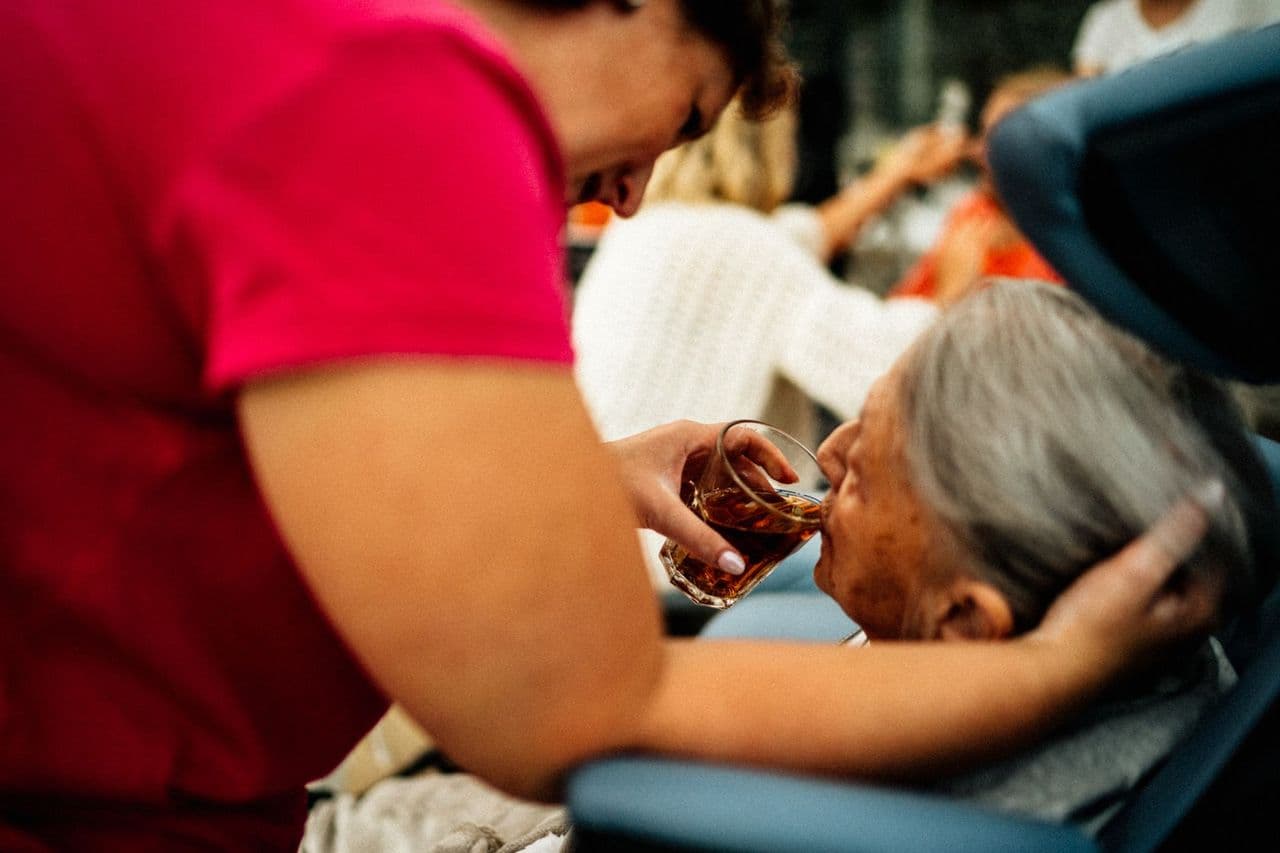 A caregiver helping an elderly woman with a drink