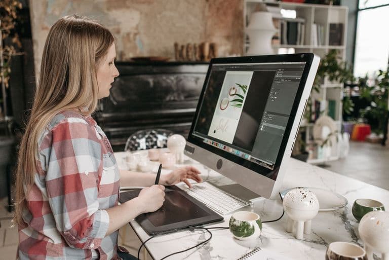 Woman using a digital drawing tablet in a stylish office workspace, focused on graphic design