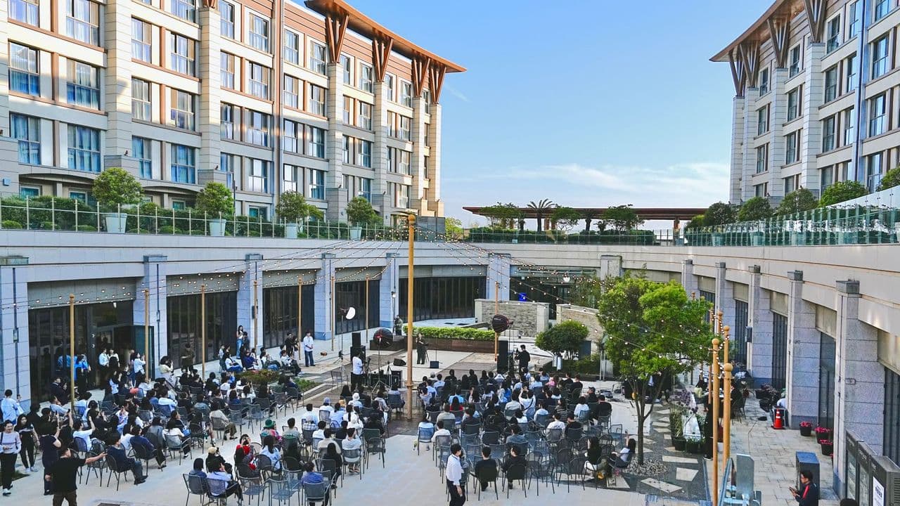 Large outdoor corporate event with attendees seated in courtyard of a modern building complex