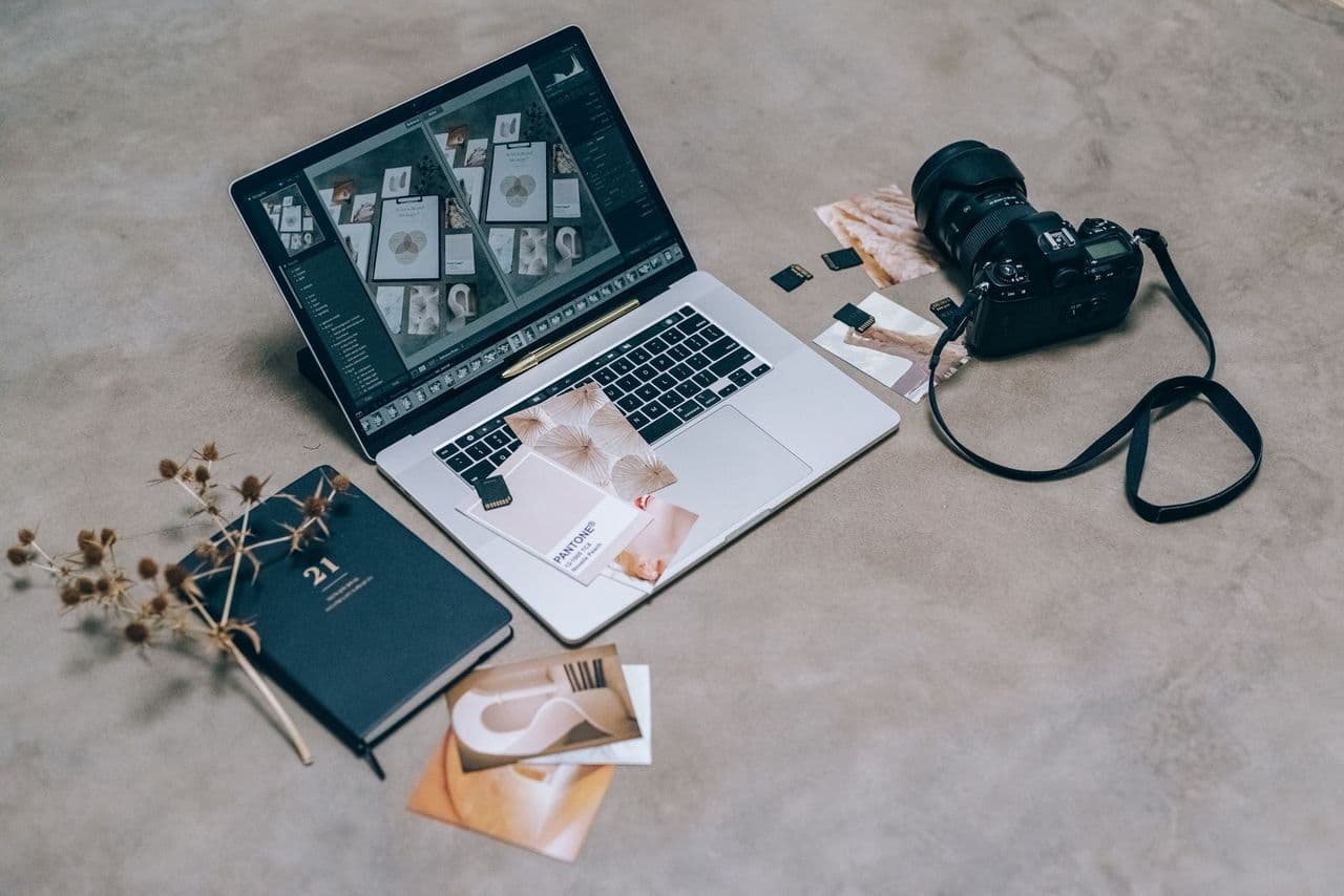 Top view of a creative workspace featuring a laptop, camera, and design materials, ideal for digital artists