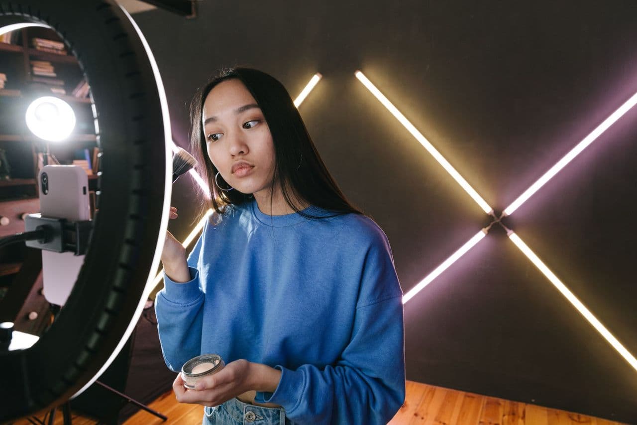Woman applying makeup under ring light in modern indoor setting, perfect for beauty content creators