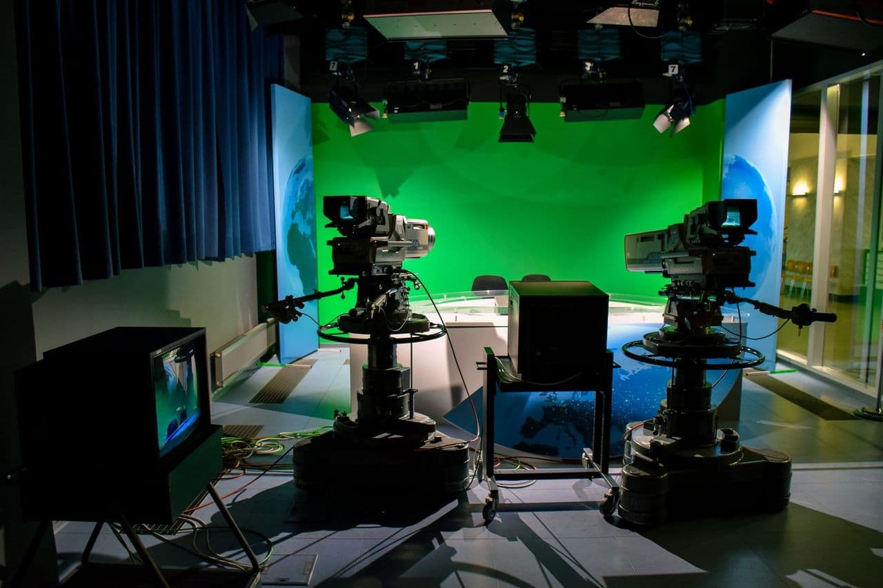 A TV studio setup featuring cameras and a green screen for production purposes