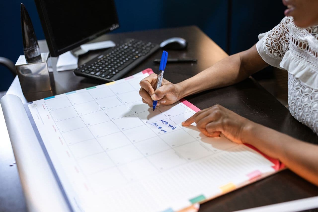 Person writing important notes in a desk calendar with a pen, set in an office