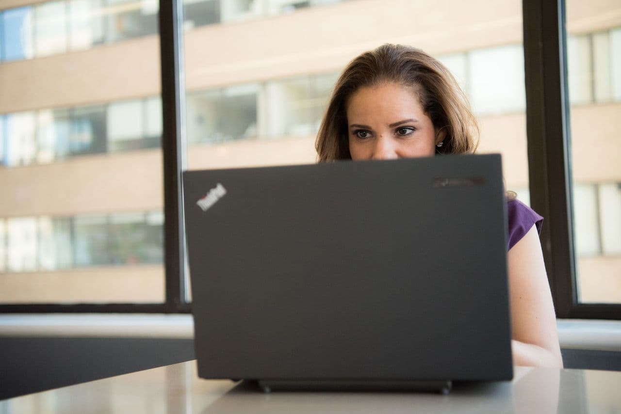 Focused woman using a laptop in a brightly lit office setting, showcasing modern work technology