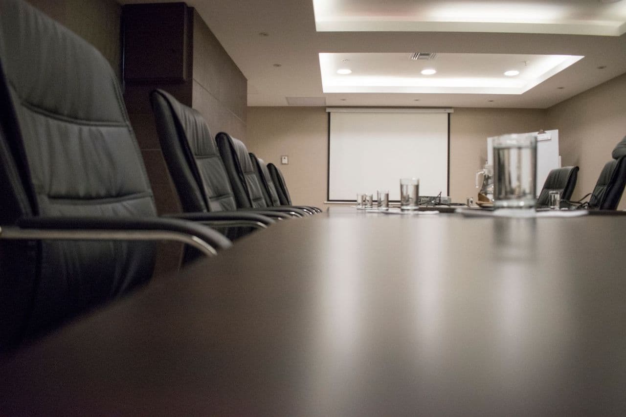 Empty conference room with black chairs, projector, and glasses on table. Ideal for business meetings