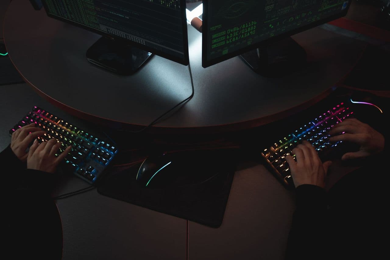 Two people typing on RGB keyboards with code on screens, indicating a cybersecurity environment