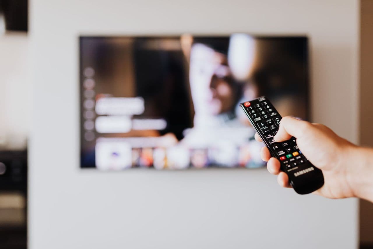 Person using a TV remote control with a blurred television screen in the background