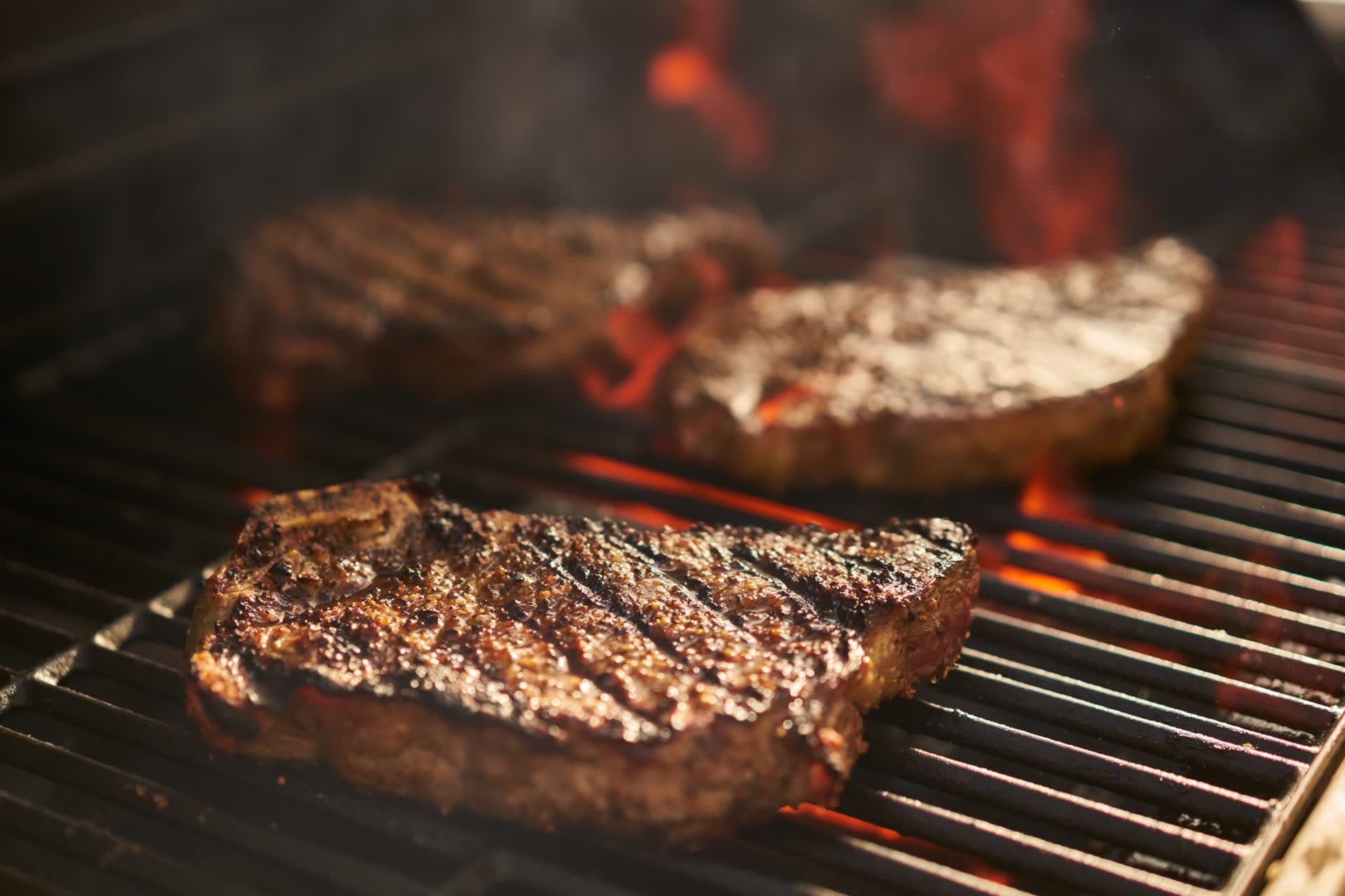 Bone-in strip steaks cooking over open flame